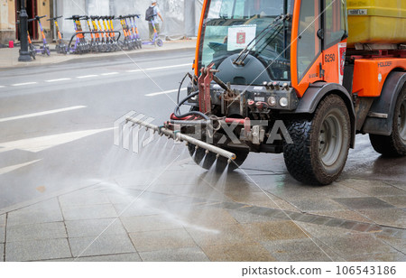 A sweeper dampens the sidewalk in the heat. A sweeper dampens the sidewalk in the heat. 106543186