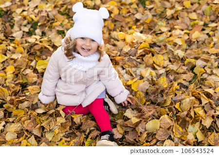 A cute pretty girl is running in the park in the middle of autumn leaves and smiling. A cute pretty girl is running in the park in the middle of autumn leaves and smiling. 106543524