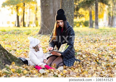 A mother is reading a book with her cute daughter while sitting on the lawn in the park 106543525