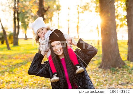 Mother and young little girl with blonde hair are playing in an autumn park on a yellow and orange leaf background 106543532