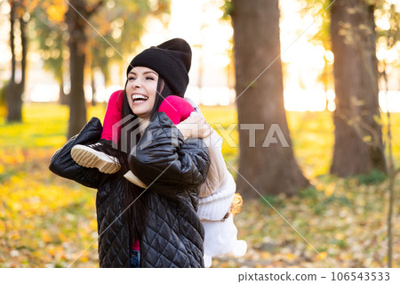 Mother and young little girl with blonde hair are playing in an autumn park on a yellow and orange leaf background 106543533