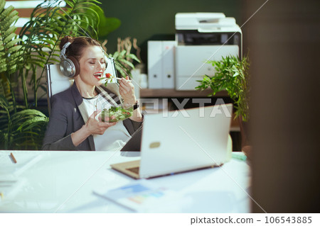 smiling female employee in green office eating salad smiling female employee in green office eating salad 106543885
