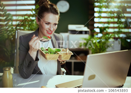 smiling business woman in green office eating salad 106543893