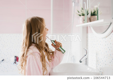 Cute girl in a pink bathrobe brushes her teeth in a bathroom hygiene concept Cute girl in a pink bathrobe brushes her teeth in a bathroom hygiene concept 106544713