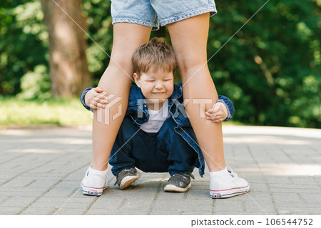 Three year old son hides under the feet of his standing mother and closes his eyes in fear. The concept of parental protection and love of your child 106544752