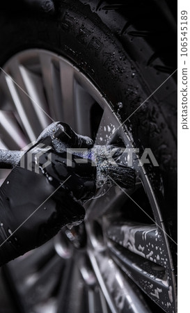 Employee of the car detailing studio or hand car wash thoroughly cleans an aluminum car wheel Employee of the car detailing studio or hand car wash thoroughly cleans an aluminum car wheel 106545189