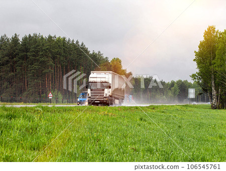 A truck with a semi-trailer transports cargo in the summer on a motorway in rainy weather. Copy space for text A truck with a semi-trailer transports cargo in the summer on a motorway in rainy weather. Copy space for text 106545761