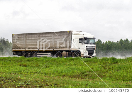 A truck with a semi-trailer transports cargo in the summer on a motorway in rainy weather. Copy space for text A truck with a semi-trailer transports cargo in the summer on a motorway in rainy weather. Copy space for text 106545770