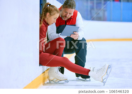 Girl, figure skating athlete with coach looking on tablet, learning techniques, watching videos on ice rink arena 106546320