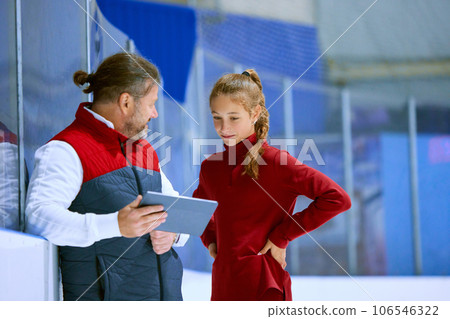 Girl, figure skating athlete with coach looking on tablet, learning techniques, watching videos on ice rink arena Girl, figure skating athlete with coach looking on tablet, learning techniques, watching videos on ice rink arena 106546322