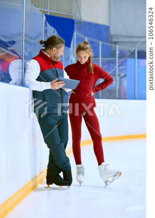 Girl, figure skating athlete with coach looking on tablet, learning techniques, watching videos on ice rink arena Girl, figure skating athlete with coach looking on tablet, learning techniques, watching videos on ice rink arena 106546324