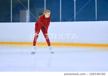 Girl in red sportswear, figure skating athlete standing on ice rink area and preparing for training session Girl in red sportswear, figure skating athlete standing on ice rink area and preparing for training session 106546380