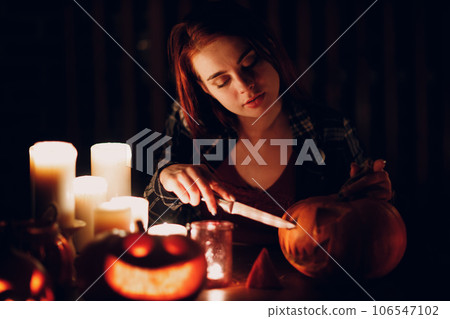 Young woman preparing Halloween pumpkin Jack-o-lantern with candles in dark. Female hands cutting pumpkins with knife 106547102