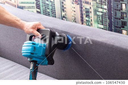 Cleaning the back of a black sofa with a special electric brush. Sofa cleaning service. Copy space for text 106547430