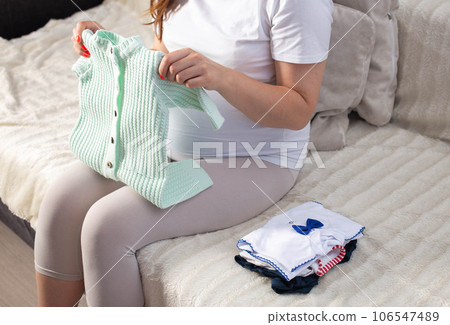 A pregnant girl collects clothes for a newborn baby in the maternity hospital. Rompers and undershirts for the baby. A pregnant girl collects clothes for a newborn baby in the maternity hospital. Rompers and undershirts for the baby. 106547489