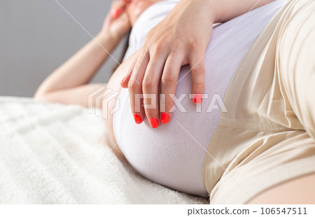 Pregnant girl lies on the couch and holds her stomach. The concept of pulling and aching pains in the abdomen of a pregnant woman due to the growth of the uterus. Copy space for text Pregnant girl lies on the couch and holds her stomach. The concept of pulling and aching pains in the abdomen of a pregnant woman due to the growth of the uterus. Copy space for text 106547511