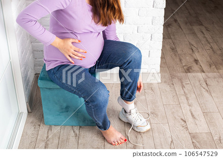 A pregnant girl puts on shoes with a big belly. Discomfort and inconvenience with bending over during pregnancy, problem. Copy space for text 106547529