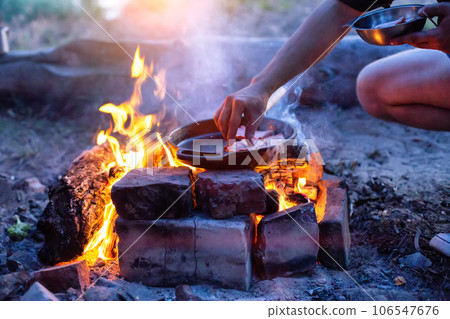 Frying bacon in a pan over a fire. Cooking outdoors in the evening. Frying bacon in a pan over a fire. Cooking outdoors in the evening. 106547676