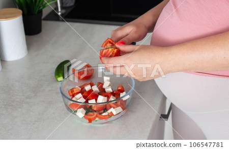A pregnant girl prepares a vegetable salad of cucumbers and tomatoes. The concept of nutrition of pregnant women with vitamins and macronutrients in vegetables. Proper nutrition. Diet during 106547781