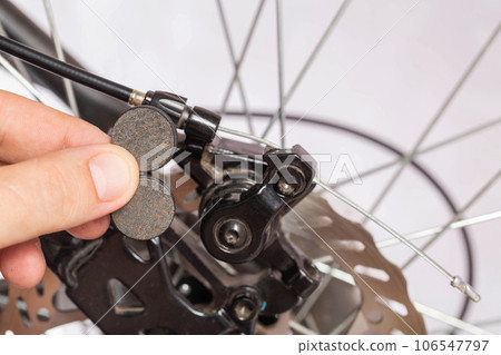 new brake pads in hand on the background of a bicycle brake caliper. Replacement of brake pads, close-up 106547797