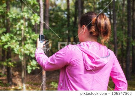 A girl in a pink sweater uses a navigator in the forest to determine her location. Mushroom picker and compass. Wandering through the forest, signal gps A girl in a pink sweater uses a navigator in the forest to determine her location. Mushroom picker and compass. Wandering through the forest, signal gps 106547803