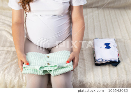 A pregnant girl arranges warm clothes for a newborn baby. Quality clothes for babies in the hospital, newborn 106548083