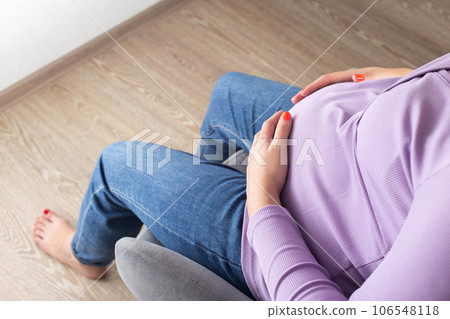 A pregnant girl sits in a chair and holds on to her stomach. The concept of fatigue and malaise during pregnancy. Uncomfortable sitting posture. A pregnant girl sits in a chair and holds on to her stomach. The concept of fatigue and malaise during pregnancy. Uncomfortable sitting posture. 106548118