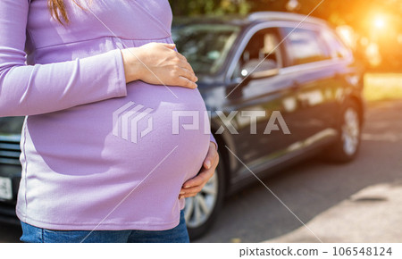 A pregnant girl with a big belly in a purple sweater on the background of a car. The concept of travel and a long trip in a car during pregnancy. Copy space for text A pregnant girl with a big belly in a purple sweater on the background of a car. The concept of travel and a long trip in a car during pregnancy. Copy space for text 106548124