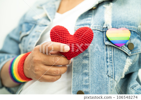 Asian lady wearing rainbow flag wristbands and hold red heart, symbol of LGBT pride month celebrate annual in June social of gay, lesbian, bisexual, transgender, human rights. 106548274