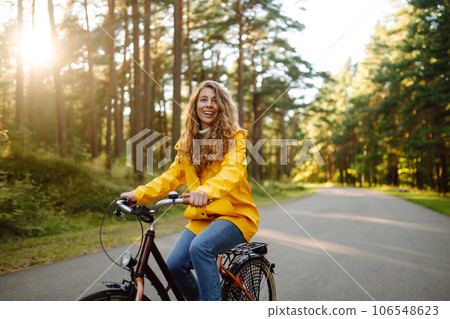 Beautiful happy woman in yellow coat riding bicycle in autumn park. Autumn fashion. Nature concept. 106548623