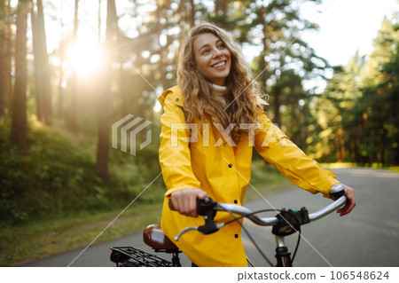 Beautiful happy woman in yellow coat riding bicycle in autumn park. Autumn fashion. Nature concept. 106548624