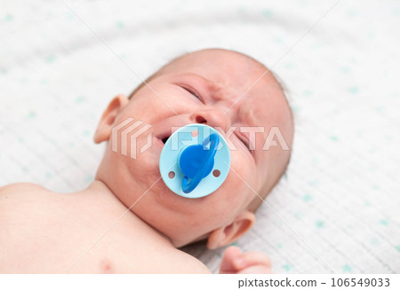 Little baby boy crying with a pacifier in his mouth. The concept of weaning the habit of sucking a pacifier in children, close-up. Copy space for text Little baby boy crying with a pacifier in his mouth. The concept of weaning the habit of sucking a pacifier in children, close-up. Copy space for text 106549033