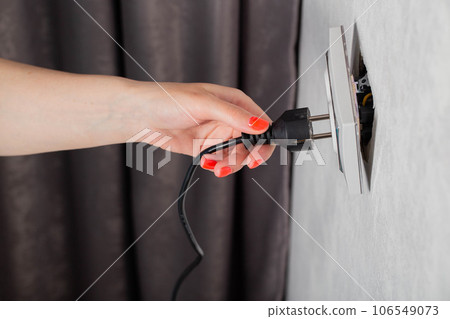 The girl removes the electrical plug from the socket and breaks the socket out of the socket. Incorrect removal of the electrical plug. Risk of electric shock, close-up The girl removes the electrical plug from the socket and breaks the socket out of the socket. Incorrect removal of the electrical plug. Risk of electric shock, close-up 106549073