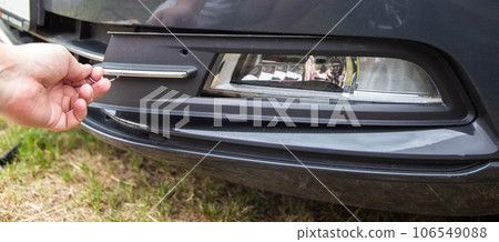 a car mechanic removes a fog lamp from a passenger car to replace a light bulb, close-up a car mechanic removes a fog lamp from a passenger car to replace a light bulb, close-up 106549088