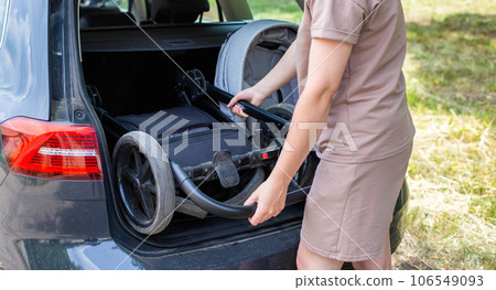 The caucasian girl puts the baby stroller in the trunk of the car. The concept of a spacious trunk in a family car. The caucasian girl puts the baby stroller in the trunk of the car. The concept of a spacious trunk in a family car. 106549093