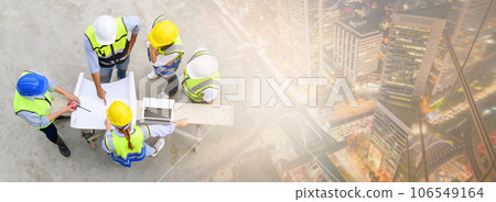 Top view of contractors, engineers and formats team in safety vests with helmets working with laptops with cityscape in night time. Banner cover design. Home building project. 106549164