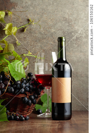 Glass and bottle of red wine with blue grapes and vine branches. 106550162