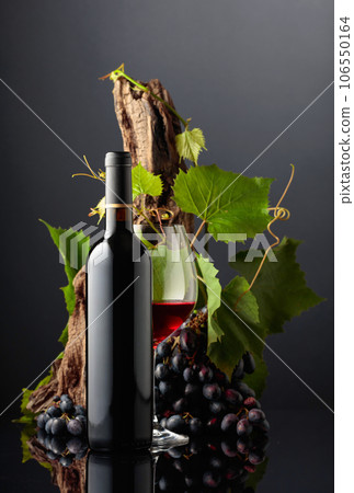 Glass and bottle of red wine with blue grapes and vine branches. 106550164
