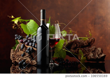 Glass and bottle of red wine with blue grapes and vine branches. 106550169