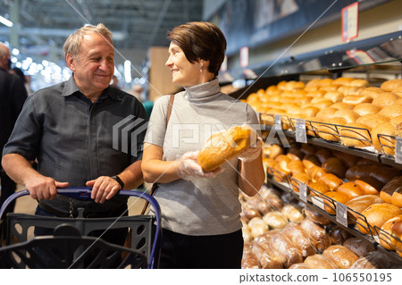 Man and woman choose hot fresh buns and bread on supermarket showcase Man and woman choose hot fresh buns and bread on supermarket showcase 106550195