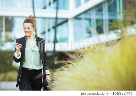 female employee in business district using phone and walking female employee in business district using phone and walking 106552745