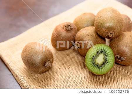 Heaps of kiwi fruit on a jute bag and sliced kiwi with visible cross-sections Heaps of kiwi fruit on a jute bag and sliced kiwi with visible cross-sections 106552776