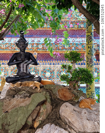 A statue of a meditating figure in a garden with orange cats and trees. A statue of a meditating figure in a garden with orange cats and trees. 106552845