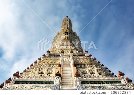 A temple in Thailand with a tall, ornate spire and a staircase leading up to it. The spire is decorated with intricate patterns and designs.The temple is made of white stone with colorful accents. A temple in Thailand with a tall, ornate spire and a staircase leading up to it. The spire is decorated with intricate patterns and designs.The temple is made of white stone with colorful accents. 106552884