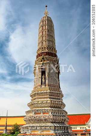 A temple in Thailand. The temple is a tall, ornate structure with many levels and intricate details. The temple is made of stone. The sky is clear blue, few clouds. 106552885