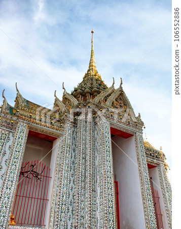 A temple in Thailand with intricate details and a tall spire. The temple has a tall spire with a golden tip and is decorated with intricate details and patterns. The sky is blue. A temple in Thailand with intricate details and a tall spire. The temple has a tall spire with a golden tip and is decorated with intricate details and patterns. The sky is blue. 106552886