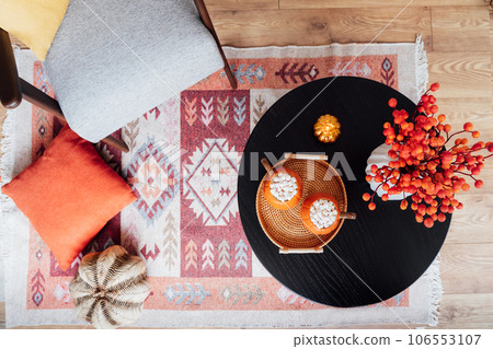 Top view pumpkin shaped cups of hot drink with marshmallows,candle and seasonal flowers on wooden table in cozy interior. Autumn beverage for Thanksgiving, Halloween holidays at home. Romantic date. 106553107
