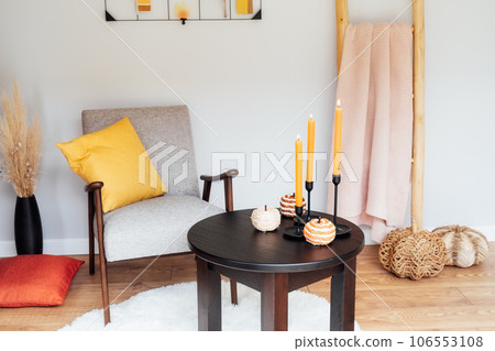 Stylish Scandinavian interior of living room with a modern armchair, coffee table with seasonal autumn decor, decorative stairs with plaid and moodboard. Cozy home interior design with a fall mood. 106553108