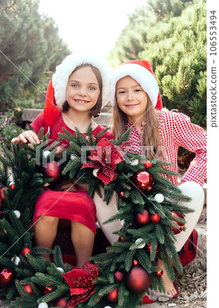 Merry Christmas. Portrait of two happy funny children girls in Santa hat with Christmas wreath. Happy Holidays. Fairy Magic. Happy kids enjoying holiday. Christmas in July 106553494