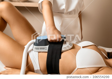 A female spa salon employee, dressed in her professional uniform, expertly performs body sculpting techniques on a client's abdominal area. 106554200